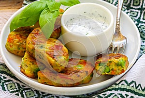 Healthy vegetarian potato patties with carrots, broccoli, bell pepper, green peas and onions with sour cream sauce with dill and