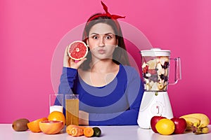 Healthy vegeterian girl openes her eyes widely, blows her mouth, looking directly at camera, holding fruit in one hand. Different photo
