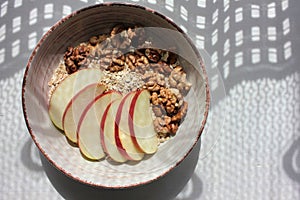 Healthy Walnut Red Apple Oatmeal in vintage bowl on white wooden table background. Natural lighting. Beautiful openwork shadow fro