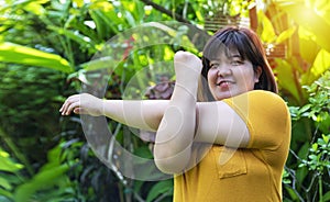 Healthy weight loss concept. Happy overweight woman stretching before workout in the garden. Fat girl obesity stretch arm