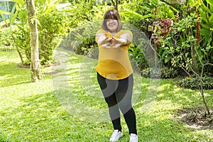 Healthy weight loss concept. Happy overweight young woman stretching before workout in the garden. Fat girl obesity stretch arm