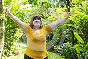 Healthy weight loss concept. Happy overweight young woman stretching before workout in the garden. Fat girl obesity stretch arm