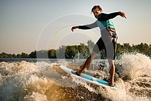 healthy wet man energetically balancing on wave on wakesurf board.