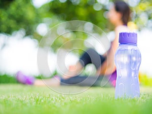 Healthy woman athlete is resting on grass. Focus on bottle of water.