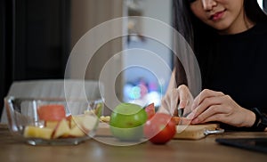 Healthy woman cutting fruits on a wooden board for making vegan salad in the kitchen. Healthy lifestyle concept