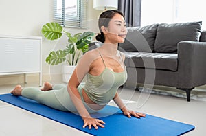 Healthy woman in green top and leggings stretching in Cobra pose or Bhujangasana on blue mat in living room at home