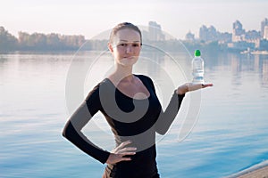 Healthy woman holds water bottle at morning river and city backround