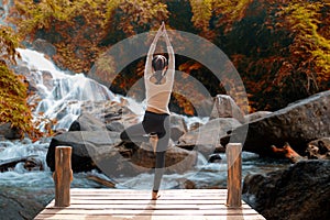 Healthy woman lifestyle balanced practicing meditate and zen energy yoga on the bridge in morning the autumn waterfall in nature.