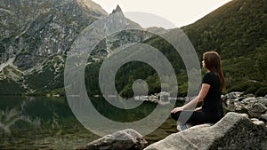 Healthy woman meditates on a mountain lake, practicing yoga, enjoys the tranquility high in the mountains