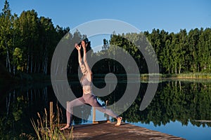 Healthy woman practicing yoga on the lake at sunrise enjoying positive energies from nature