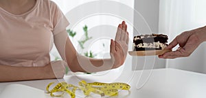 A healthy woman pushes a plate into a chocolate cake. Abstain from eating sweets and diet concept