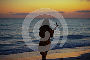Healthy woman on seashore at sunset holding starfish