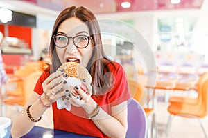 Healthy woman sitting in indoors food court and eating an delicious hamburger, modern meal concept