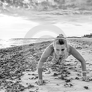 Healthy woman in sport clothes on beach doing pushups