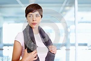 Healthy woman taking a break from workout. Woman with towel and water bottle looking away during a break from workout.