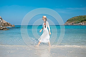 A healthy woman in a white dress walks on the beach