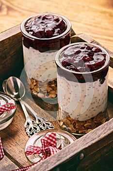 Healthy yogurt dessert wih chia seeds, muesli and jellied berries on wooden tray.