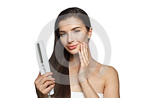 Healthy young adult woman using hair iron and straightening her long brown hair on white background, studio fashion beauty