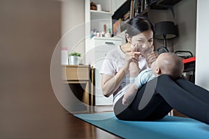 Healthy Young Asian mother sitting playing with her little cute baby boy son while practicing yoga and exercising on yoga mat at