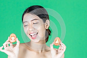 Healthy young Asian woman holding fresh tomato slice over green isolated background. Healthy and beauty skin care concept