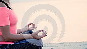 Healthy, young beautiful woman meditating, practicing yoga on the beach, by the sea, at sunrise, Relaxes muscles, mind