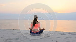 Healthy, young beautiful woman meditating, practicing yoga on the beach, by the sea, at sunrise, Relaxes muscles, mind