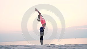 Healthy, young beautiful woman meditating, practicing yoga among the sand, on the beach, by the sea, river, at dawn, at