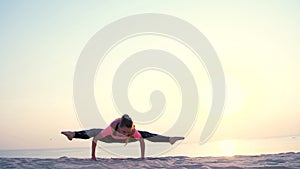 Healthy, young beautiful woman meditating, stretching, practicing yoga on the sea beach, at sunrise, Makes exercises for