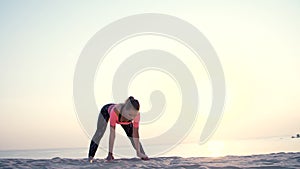 Healthy, young beautiful woman meditating, stretching, practicing yoga on the sea beach, at sunrise, Makes exercises for