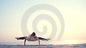 Healthy, young beautiful woman meditating, stretching, practicing yoga on the sea beach, at sunrise, Makes exercises for