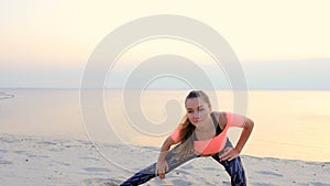 Healthy, young beautiful woman meditating, stretching, practicing yoga on the sea beach, at sunrise, Makes exercises for