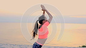 Healthy, young beautiful woman meditating, stretching, practicing yoga on the sea beach, at sunrise, Makes exercises for