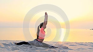 Healthy, young beautiful woman meditating, stretching, practicing yoga on the sea beach, at sunrise, Makes exercises for