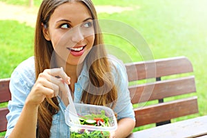 Healthy young business woman eating salad in the park and looking to the side the copy space area