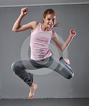 Healthy young muscular teenage girl skipping and dancing in studio. Child exercising with jumping on grey background.