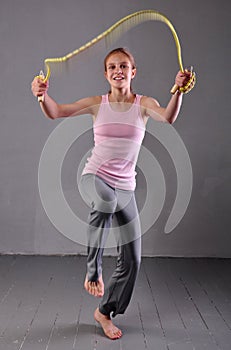 Healthy young muscular teenage girl skipping rope in studio. Child exercising with jumping on grey background.