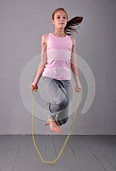 Healthy young muscular teenage girl skipping rope in studio. Child exercising with jumping on grey background.