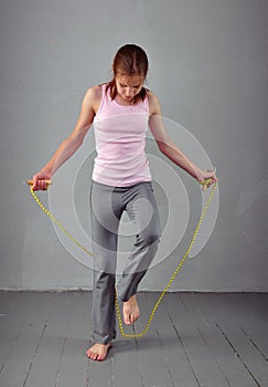 Healthy young muscular teenage girl skipping rope in studio. Child exercising with jumping high on grey background.