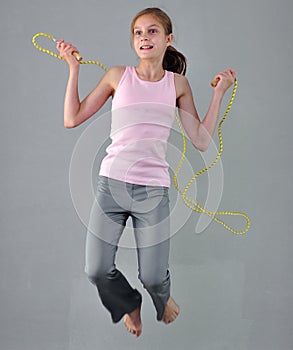 Healthy young muscular teenage girl skipping rope in studio. Child exercising with jumping high on grey background.