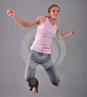 Healthy young muscular teenage girl skipping rope in studio. Child exercising with jumping high on grey background.