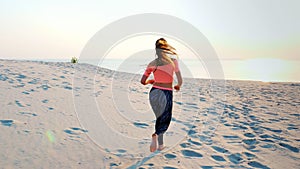 Healthy, young sports beautiful woman runs along the sand, on the beach, in summer, towards the sun, at the sunrise.