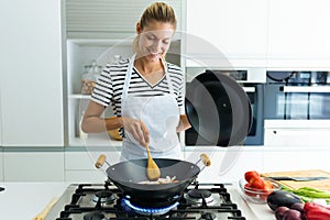 Healthy young woman cooking and mixing food in frying pan in the kitchen at home.