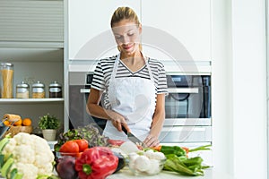 Healthy young woman cutting fresh vegetables in the kitchen at home.