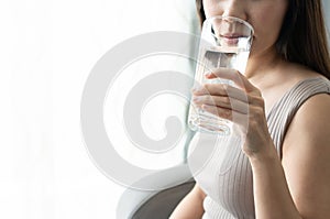 Healthy young woman enjoying fresh clean water while sitting on sofa at home. To drink enough daily amount of water to moisten the