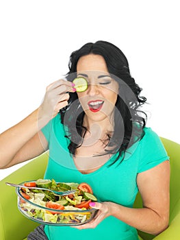 Healthy Young Woman Holding a Fresh Bowl of Mixed Colourful Salad Holding A Cucumber Slice Over Her Eye