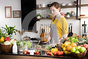 Healthy young woman in a kitchen preparing fruits and vegetables for healthy meal and salad