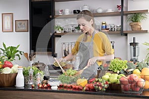 Healthy young woman in a kitchen preparing fruits and vegetables for healthy meal and salad