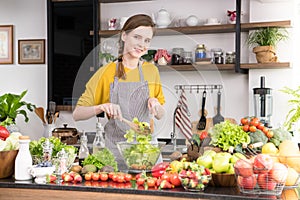 Healthy young woman in a kitchen preparing fruits and vegetables for healthy meal and salad