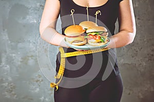 Healthy young woman looking at healthy and unhealthy plates of food, trying to make the right choice