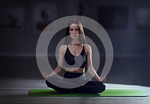 Healthy young woman practicing yoga and sitting in padmasana at training hall